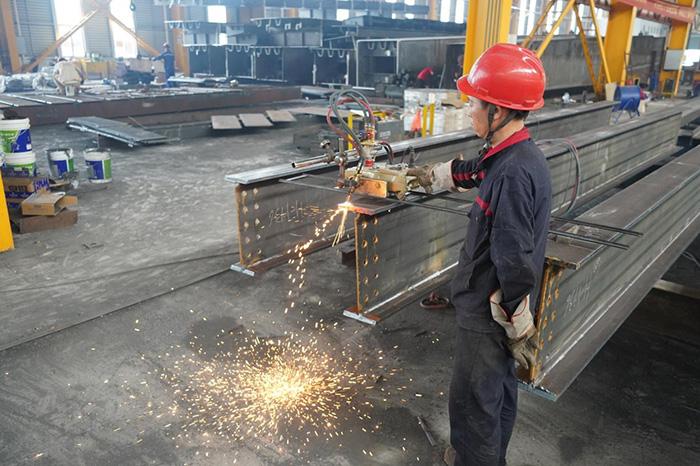 Durante el proceso de producción de vigas H en el taller de estructuras de acero, los trabajadores utilizan una máquina cortadora de llama orbital automática para cortar las ranuras.
