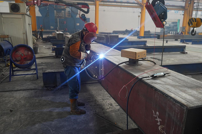 Durante el proceso de producción de puentes con estructura de acero, los trabajadores sueldan los componentes de las vigas de cajón de acero utilizando soldadura protegida con gas de dióxido de carbono.