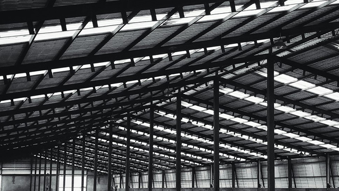 Vista interior de un almacén con estructura ligera de acero, cerchas de acero en el techo y columnas de soporte verticales.