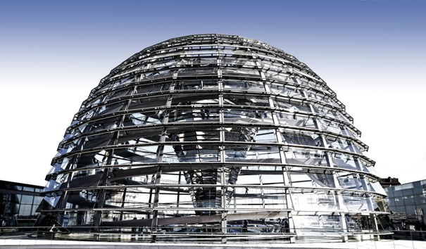 Vista interior de un enorme atrio de acero y vidrio con una estructura expuesta y escaleras mecánicas que conducen a un espacioso salón.